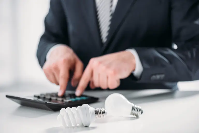 Businessman calculating energy costs with light bulbs