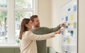 HR manager reviewing wall calendar with absence markers alongside team member, UK office