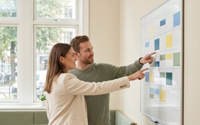 HR manager reviewing wall calendar with absence markers alongside team member, UK office