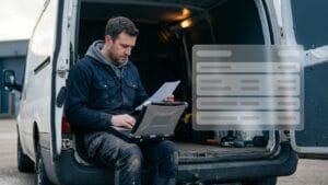 A contractor sitting on the tailgate of his van with a rugged laptop on his knees, reading a document, with a translucent data panel floating beside him